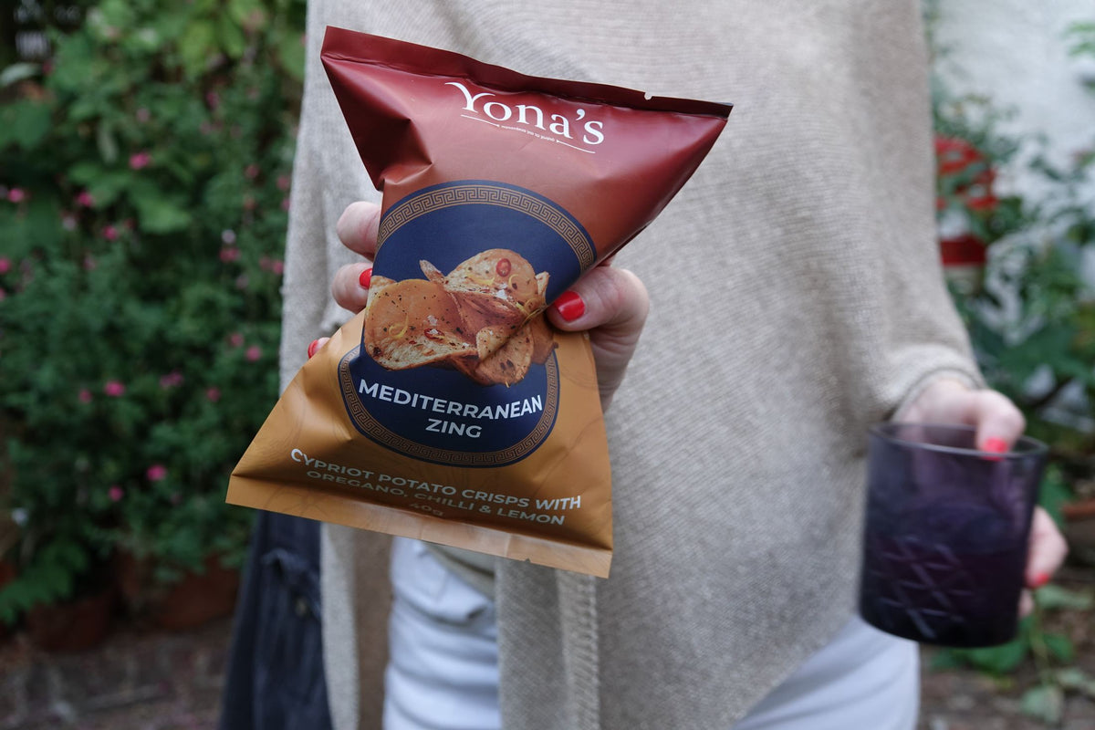 A 140g bag of Mediterranean Zing held up in a garden, drink in the other hand