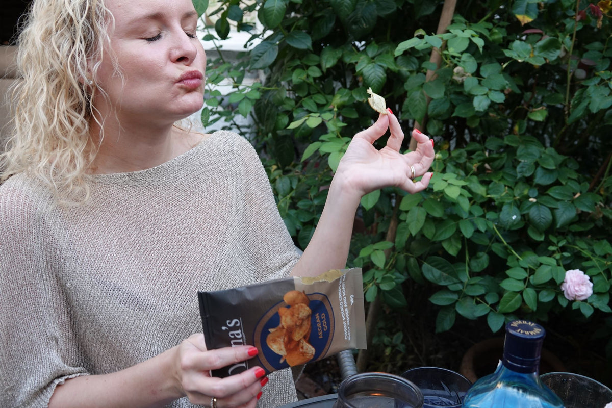 A woman savouring a crisp in a rose garden, eyes closed, holding a bag of Aegean Gold